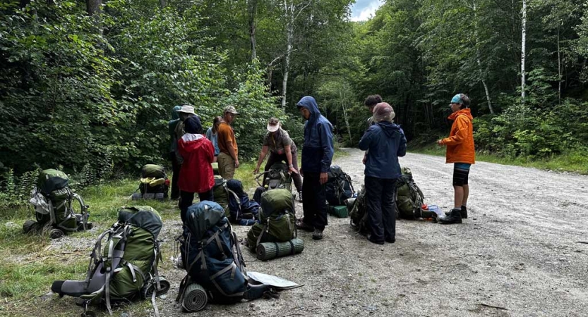 A group of teens take a break from backpacking with their packs resting on the ground. 